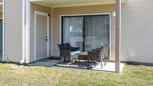 A covered patio with a sliding glass door, outdoor furniture, and a door to the building. - Cozy 1-bedroom condo with AC, WiFi in charming Little River. 3 miles from beach. (Little River)
