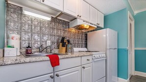 A kitchen with white cabinets, a granite countertop, a stainless steel range hood, and a white refrigerator. - Cozy 1-bedroom condo with AC, WiFi in charming Little River. 3 miles from beach. (Little River)