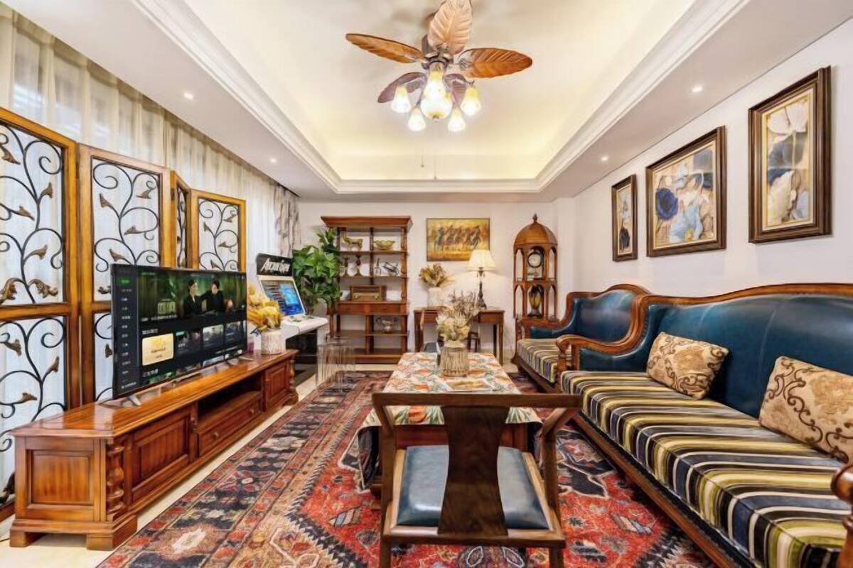 Un salon spacieux doté d’un grand téléviseur à écran plat, d’un meuble de rangement en bois, d’un canapé bleu, d’un tapis à motifs et d’un ventilateur de plafond.