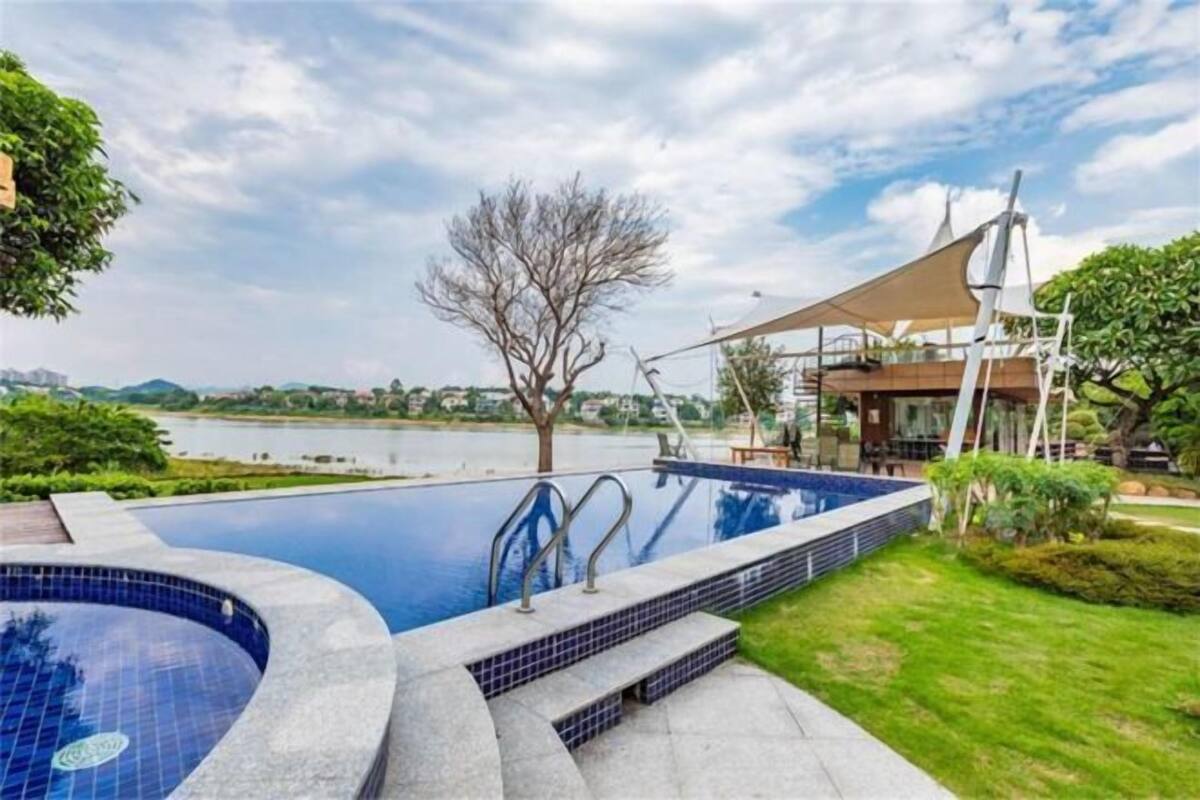 Une piscine avec vue sur un lac, entourée de verdure et bordée d’un bâtiment au design moderne.