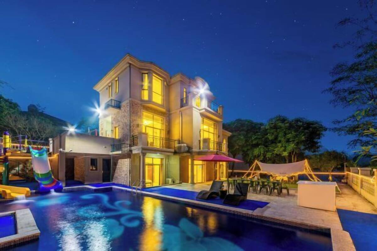 Une maison à deux étages avec une piscine, un espace salon extérieur et un toboggan.