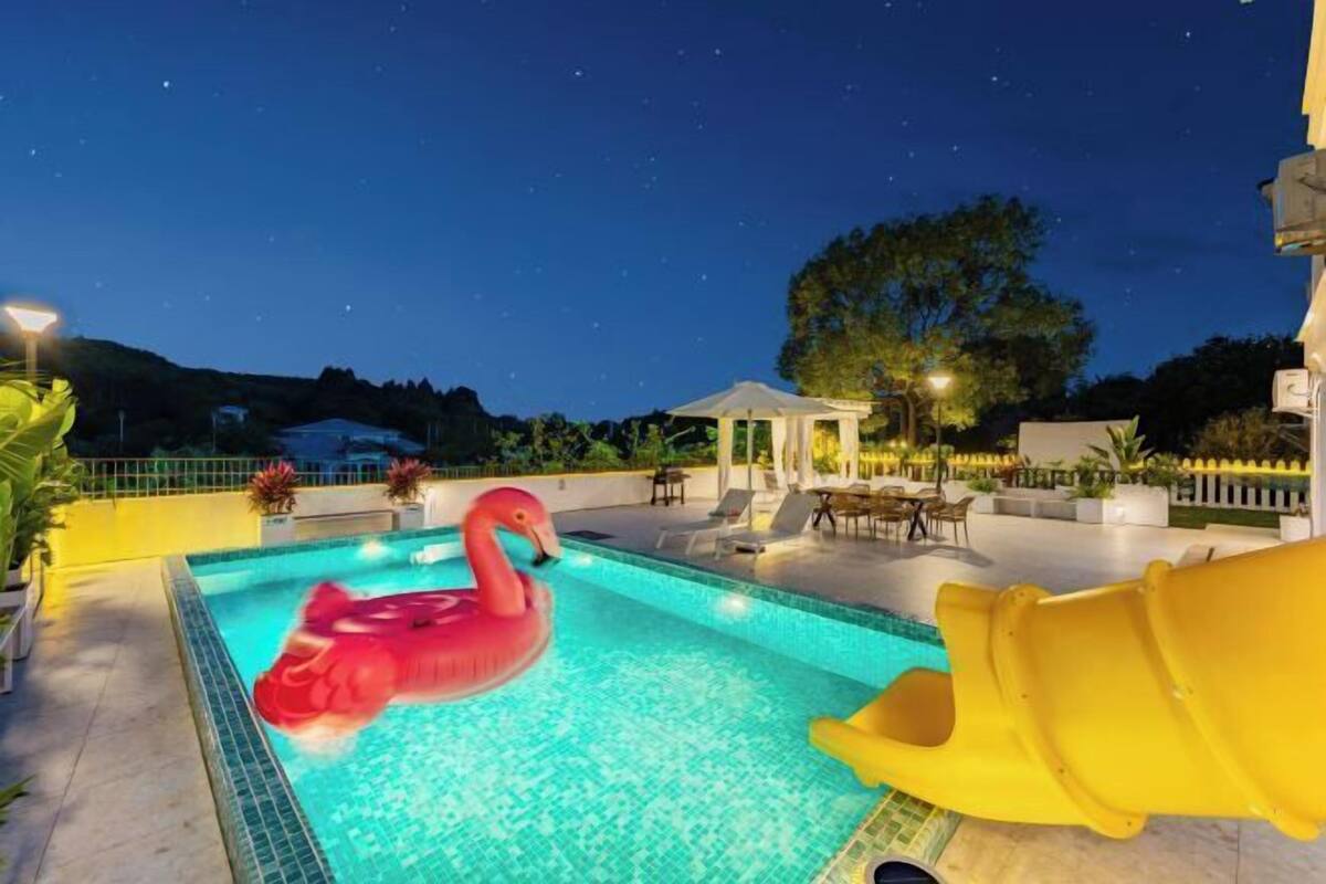 Une piscine avec un flotteur en forme de flamant rose, un toboggan et des espaces de détente en plein air.