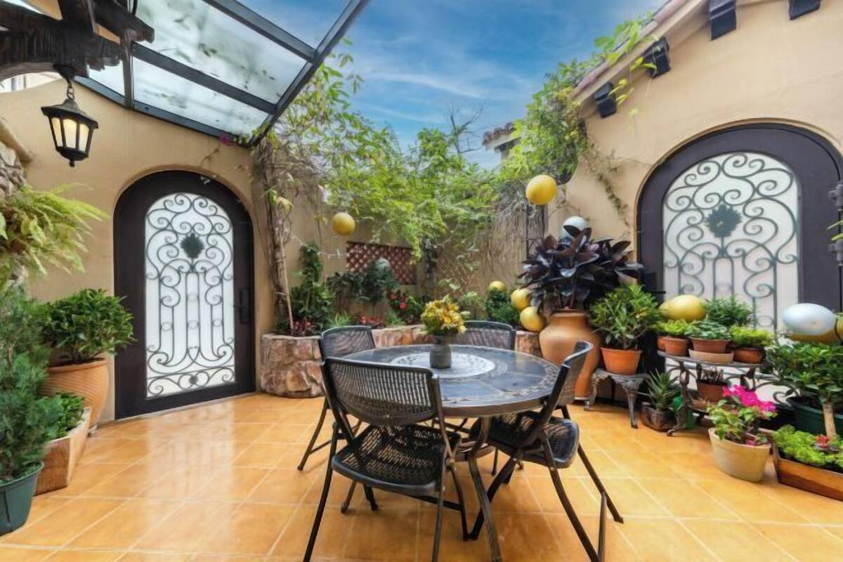 Une terrasse avec une table ronde et des chaises, entourée de plantes en pot et d’une clôture décorative.