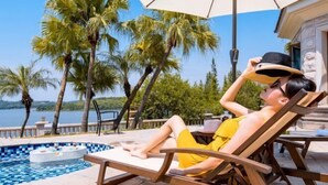 Un espace aménagé au bord de la piscine, avec un fauteuil de relaxation, un jacuzzi et une vue sur les palmiers et l’eau.