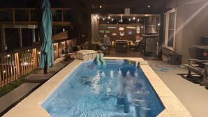 A swimming pool with a wooden deck and lounge chairs.