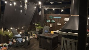 An outdoor patio area with a grill, lounge chairs, string lights, and a sign indicating pool rules.