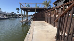A wooden dock extending into calm water with a covered seating area and a staircase leading to a higher platform.