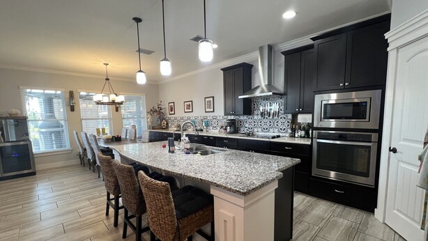 A modern kitchen with a large island, dark cabinetry, stainless steel appliances, and a dining area with wicker chairs.