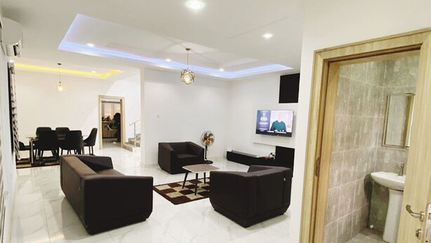 A spacious living area with a modern design, featuring a flat-screen TV, comfortable seating, and a clean, tiled floor. - Merryway Apartment (Abuja)