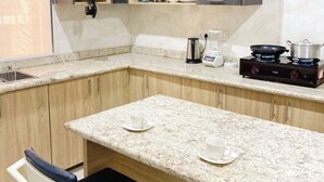 A compact kitchen with granite countertops, a gas stove, a coffee maker, and a sink. There are two chairs and a small island with two cups. - Merryway Apartment (Abuja)