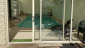 Una piscina vetrata con area prendisole, comprensiva di una sedia e un tavolino.