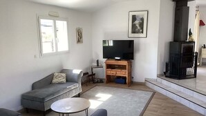 Un soggiorno con un divano grigio, un tavolino rotondo, un televisore su un supporto in legno e un camino.