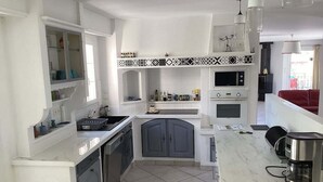 Una cucina moderna con mobili bianchi, forno integrato, microonde e macchina per il caffè sul piano di lavoro.