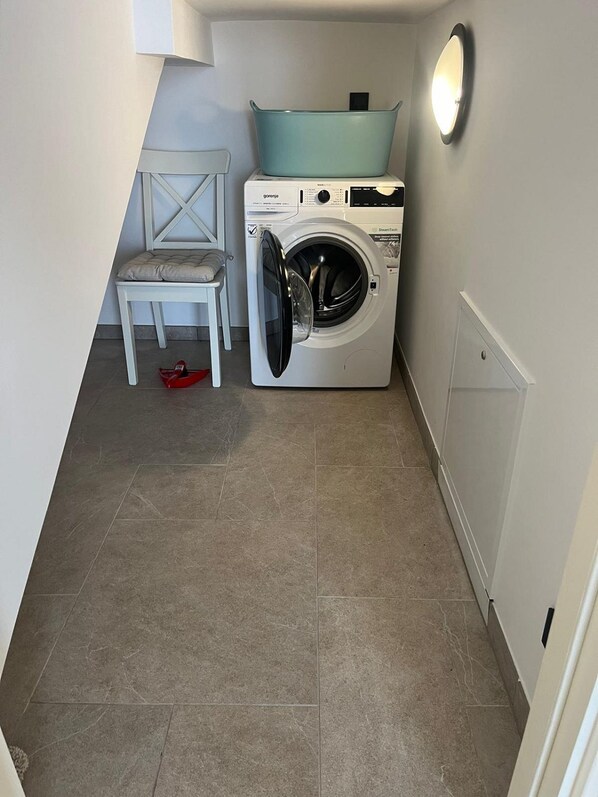 A laundry room with a front-loading washing machine, a chair, and a small table.