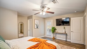 A bedroom with a bed, a ceiling fan, a TV, a door, and a window. - Spacious 4BR/2.5BA Houston Home, Pool, WiFi & AC Included (Houston)