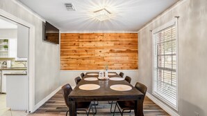 A dining area with a wooden wall panel, a dark wooden table, and a ceiling light fixture. - Spacious 4BR/2.5BA Houston Home, Pool, WiFi & AC Included (Houston)