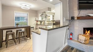 A modern kitchen with a central island, bar stools, a fireplace, and a TV mounted on the wall. - Spacious 4BR/2.5BA Houston Home, Pool, WiFi & AC Included (Houston)