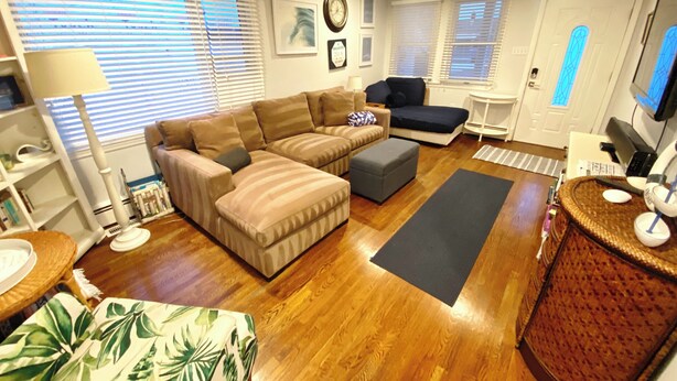 A living room with a sectional sofa, ottoman, and a coffee table. There is a television, a desk with a computer, and a chair.