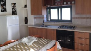 Une cuisine de taille réduite, avec des meubles en bois, un réfrigérateur blanc, une cuisinière à gaz et une fenêtre au-dessus de l’évier.