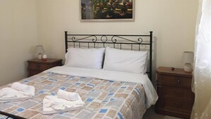 Un lit bien fait, recouvert d’une couvre-lit à motifs, avec un tableau accroché au-dessus, une table de chevet avec une lampe et une petite table placée à côté du lit.