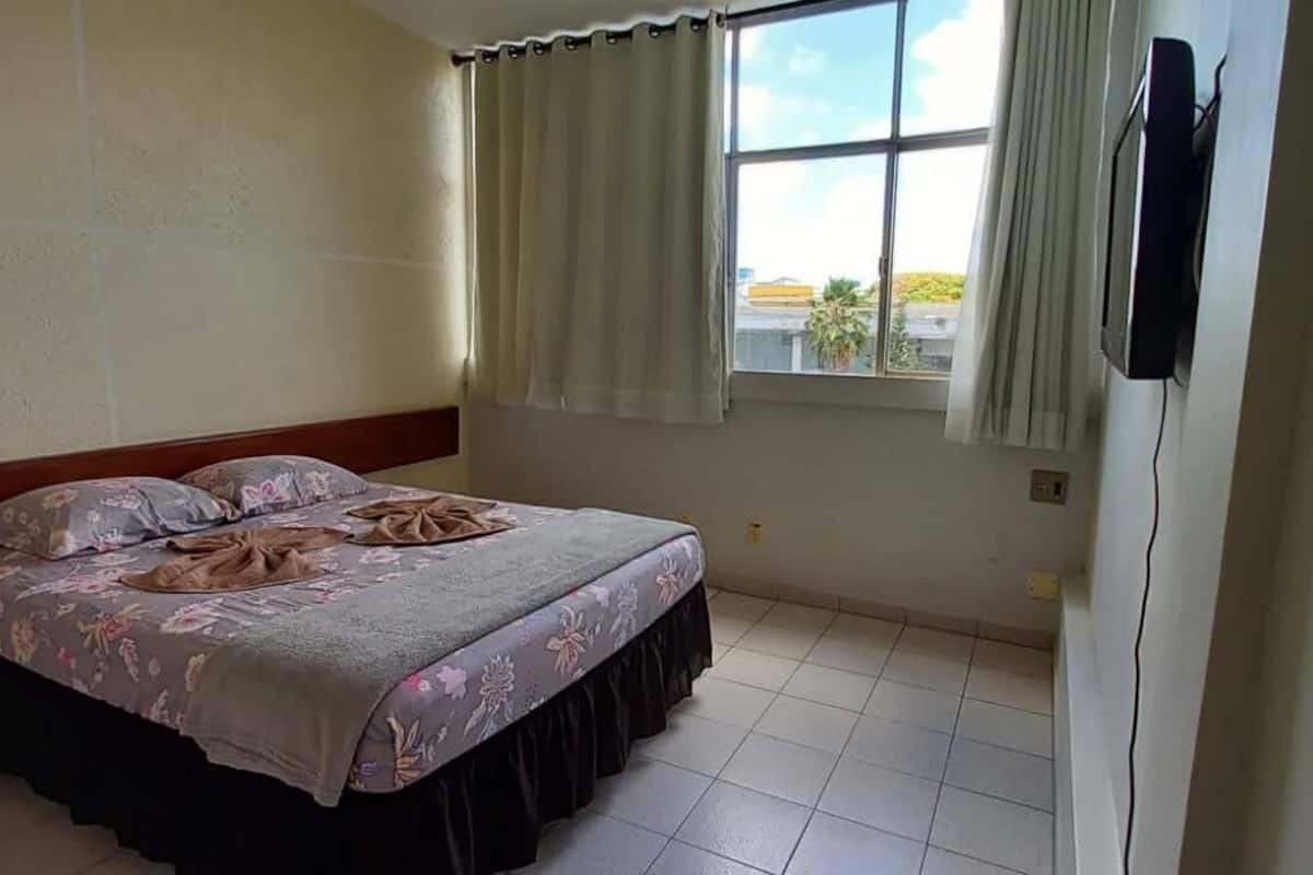 Une chambre à coucher avec un lit, des rideaux, une fenêtre et un téléviseur fixé au mur.