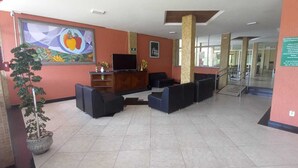 A reception area with a reception desk, seating, a potted plant, and a painting on the wall. - Hotel Fenix (Aracaju)