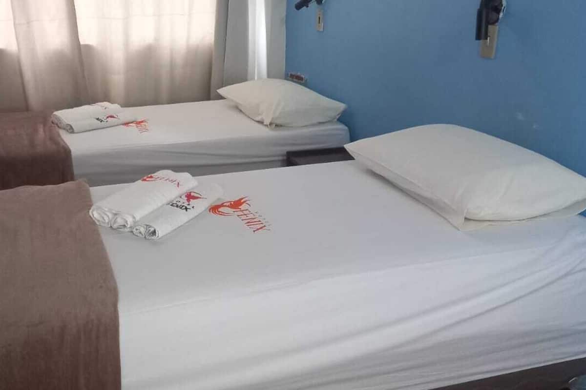 Une chambre d’hôtel avec deux lits simples, chacun recouvert d’une courtepointe blanche et agrémenté d’une serviette roulée.