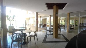 A spacious indoor area with a restaurant in the background, a tiled floor, and several tables and chairs. - Hotel Fenix (Aracaju)