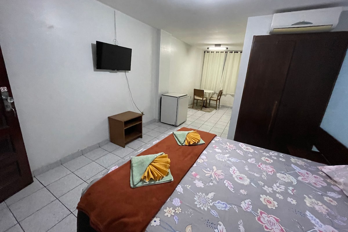 Une chambre d’hôtel avec un lit, un téléviseur fixé au mur, un petit bureau et une chaise.