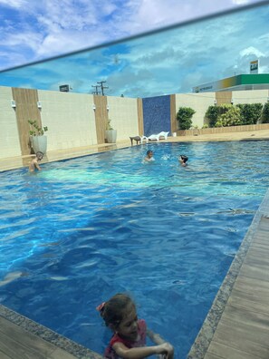 A swimming pool with clear blue water, surrounded by a tiled deck and a wooden fence. - Hotel Fenix (Aracaju)