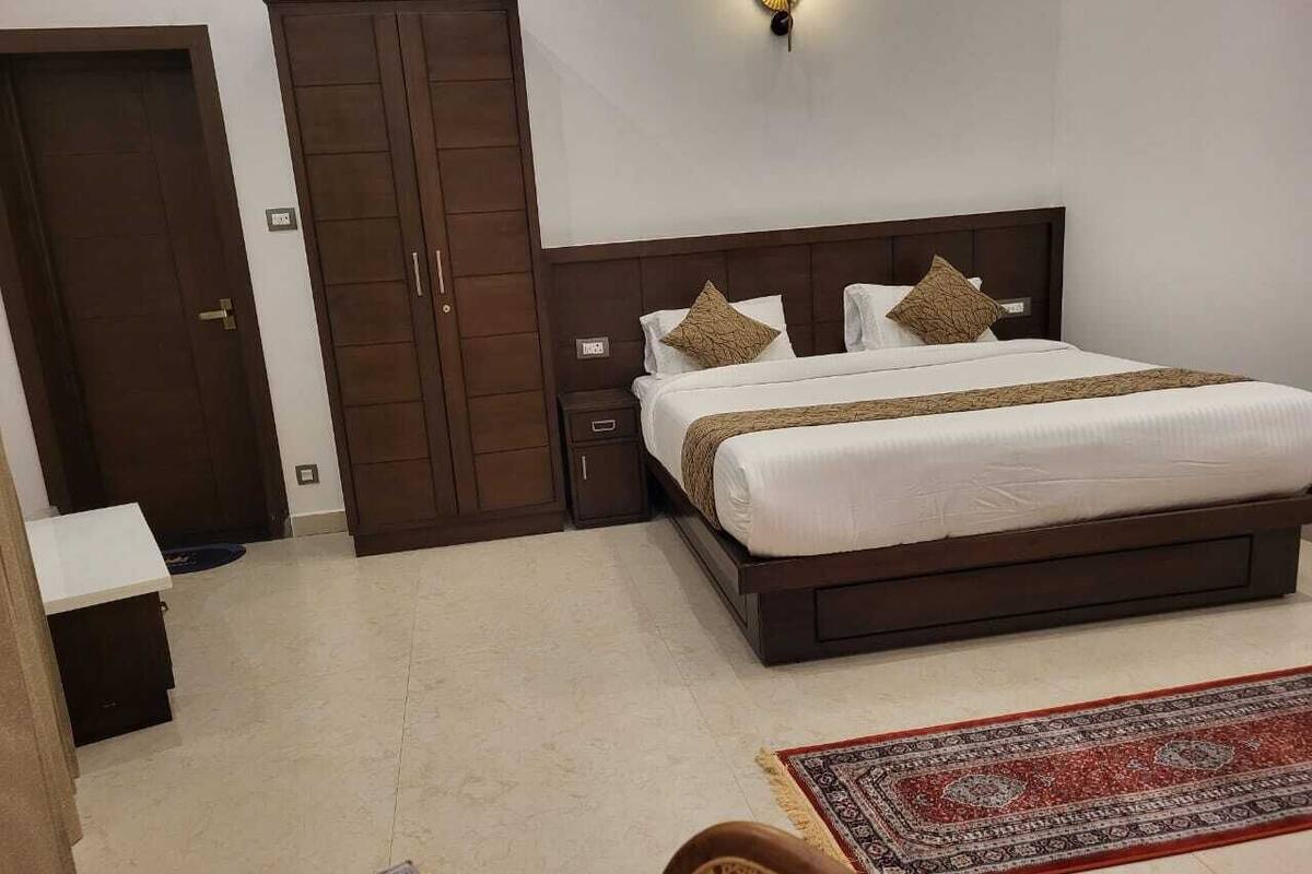 A bedroom with a large bed, a wardrobe, a bedside table, and a wall-mounted light fixture.