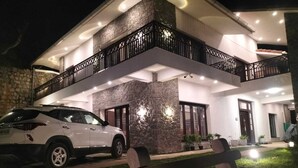 A modern two-story house with a stone facade, a white car parked in front, and a well-lit entrance. - Glen Mist (Kodaikanal)