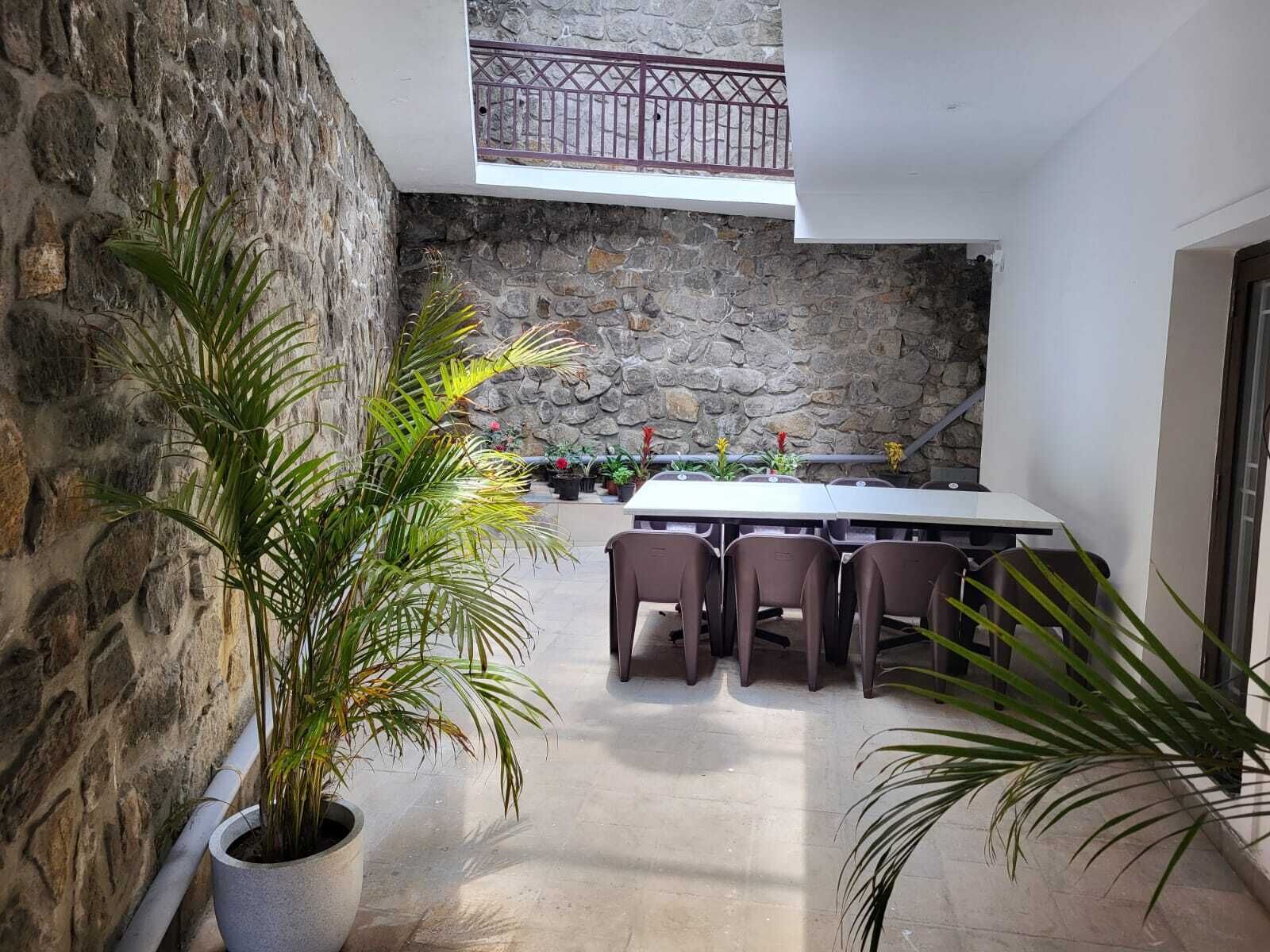 Un patio con pareti in pietra, un tavolo e sedie, piante in vaso e un balcone con ringhiera.