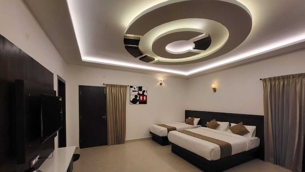 A modern hotel room with a large bed, a flat-screen TV, and a ceiling with circular light fixtures. - Glen Mist (Kodaikanal)