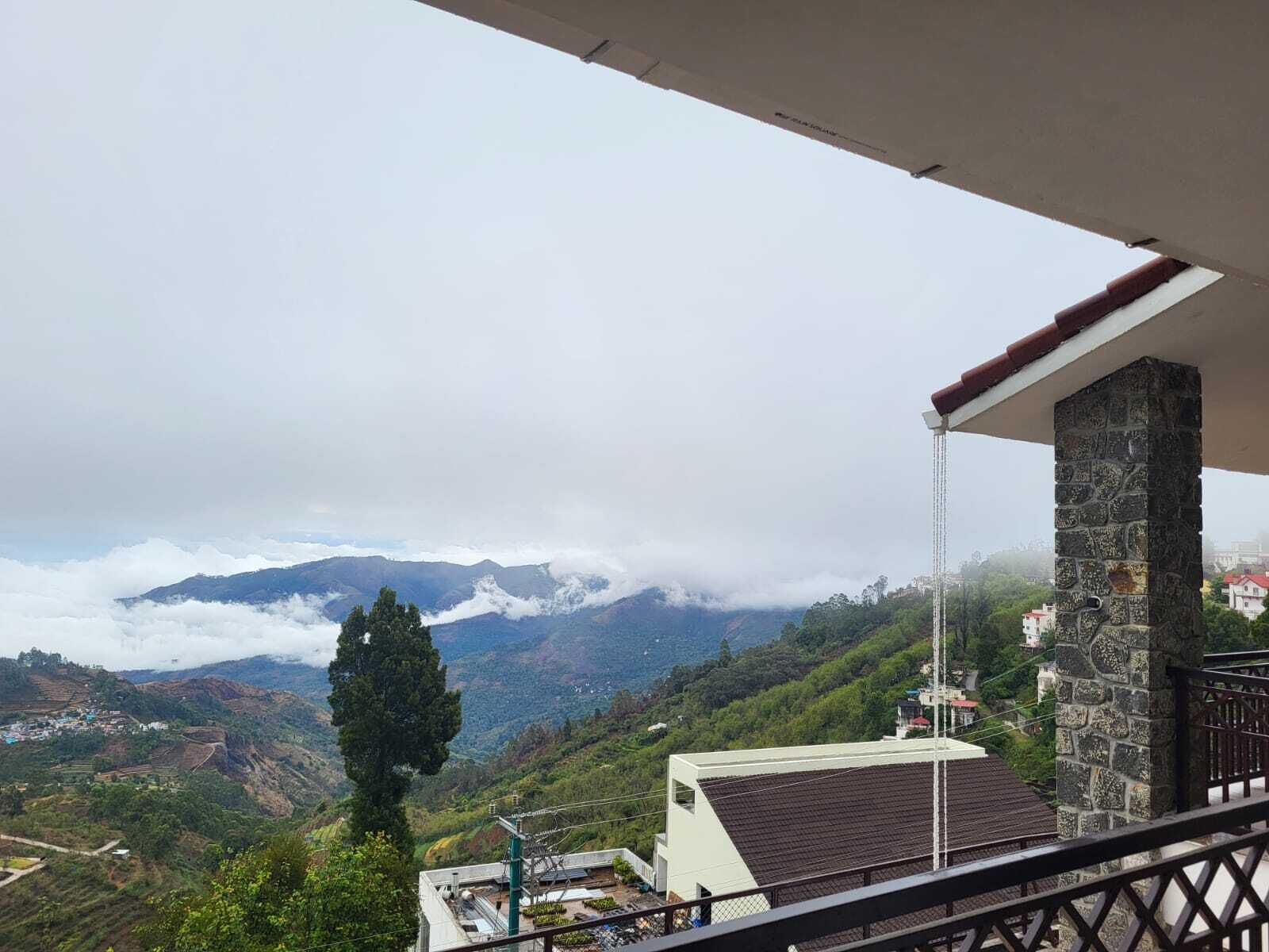 Uma varanda com um pilar de pedra, com vista para uma paisagem montanhosa com campos em socalcos e uma aldeia abaixo.