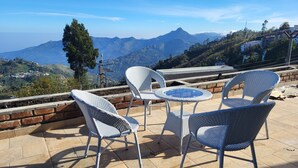 A terrace with wicker chairs and a table, overlooking a mountainous landscape. - Glen Mist (Kodaikanal)