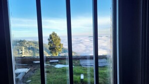 A view through a window with vertical blinds, featuring a landscape with a tree and distant hills. - Glen Mist (Kodaikanal)