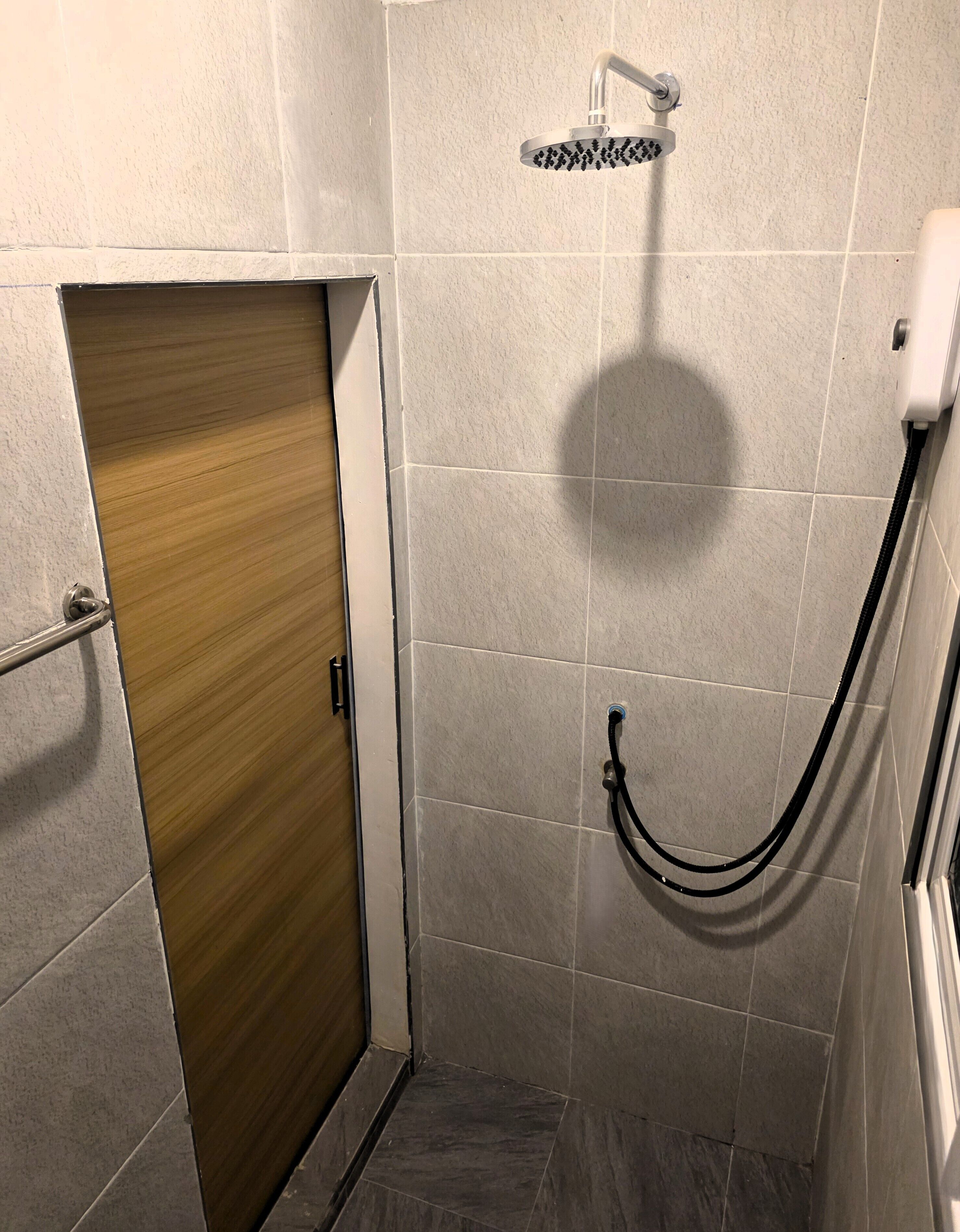 A small, tiled shower area with a wooden door and a showerhead.