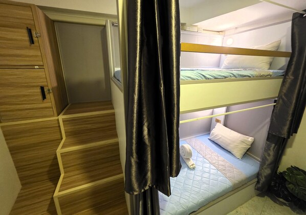 A bunk bed with a quilted mattress, a wooden wardrobe, and a staircase. - Hideout Hostel 2 (Ko Pha-ngan)