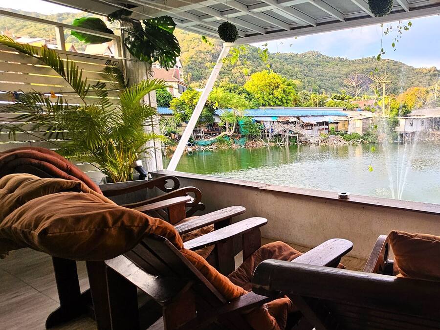 Restaurante con terraza al aire libre que da a un cuerpo de agua, con mesas y sillas de madera y cojines.