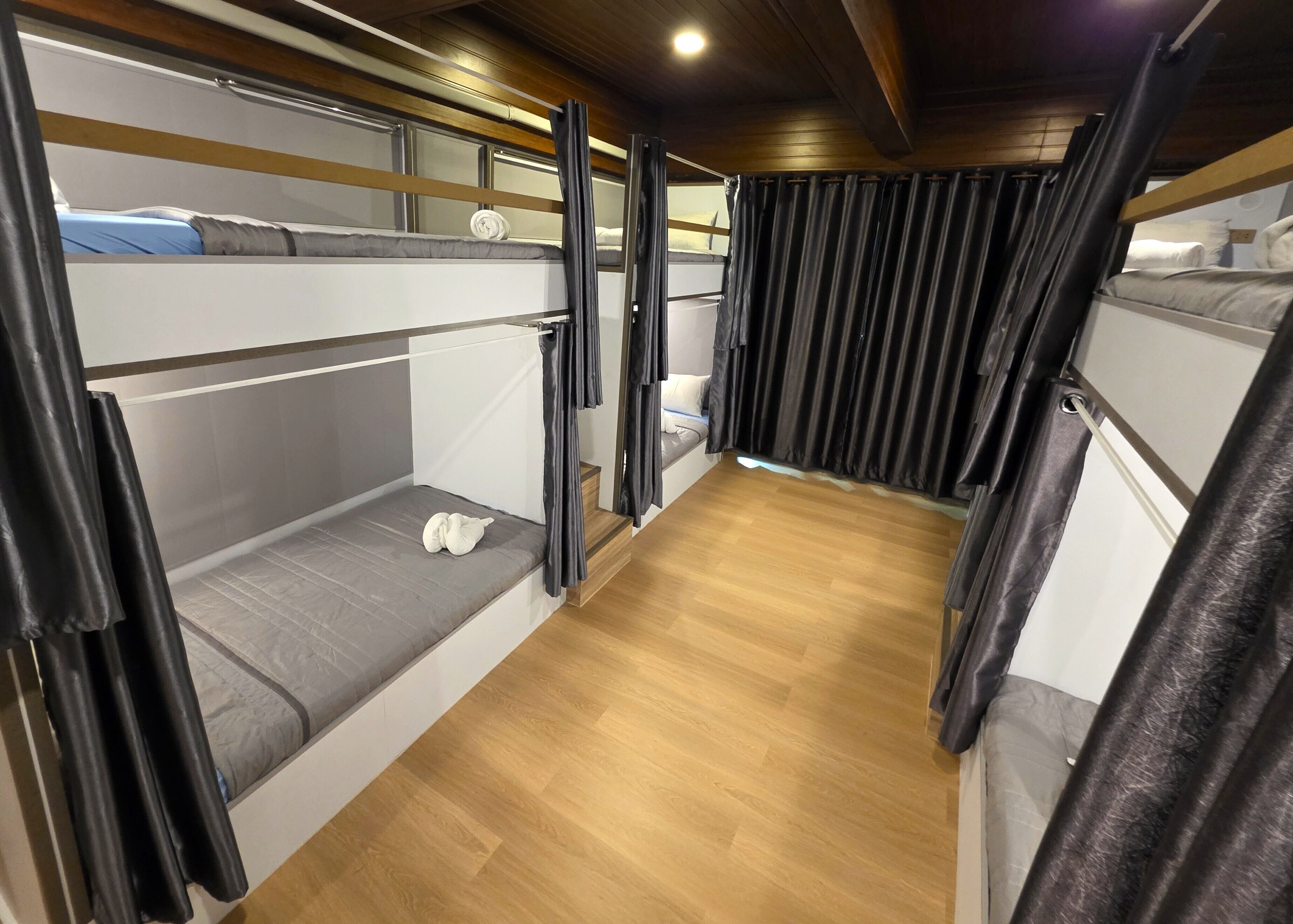 Habitación pequeña y bien iluminada con literas, suelo de madera y cortinas.