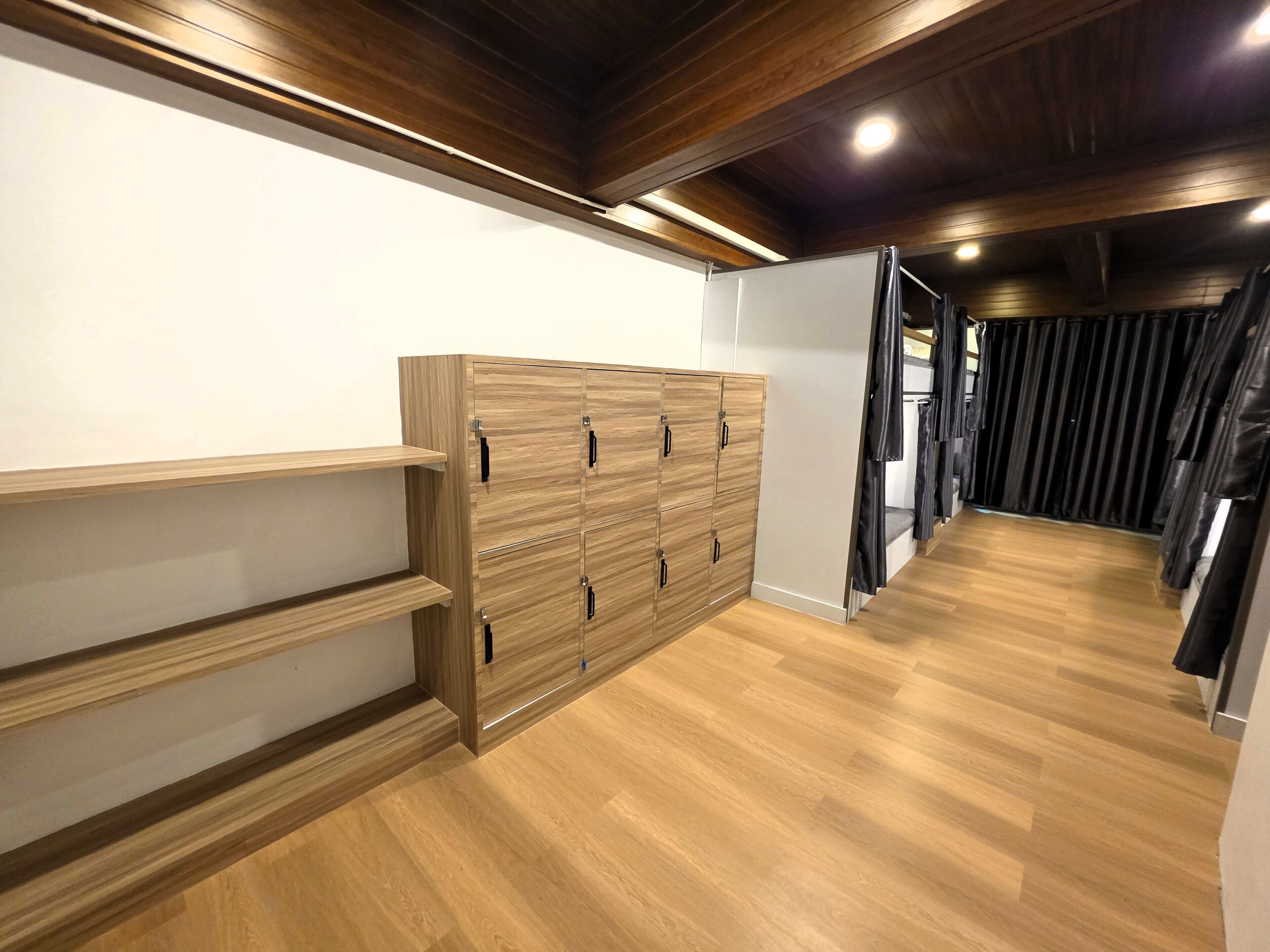 Un pasillo con suelo de madera, un armario de madera con múltiples puertas y un banco con cortinas negras.