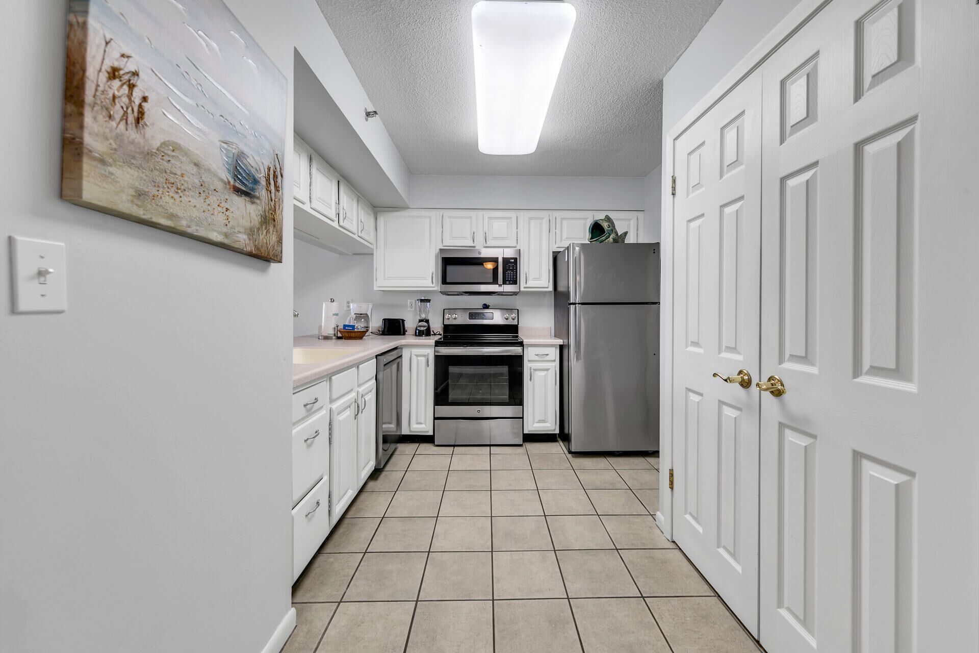A kitchen with white cabinets, a microwave, a refrigerator, and a painting on the wall.