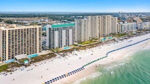 A beachfront hotel with multiple high-rise buildings, a sandy beach with umbrellas, and a clear view of the ocean.