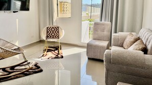 A modern living room with a sofa, a chair, a flat-screen TV, and a large window with curtains.