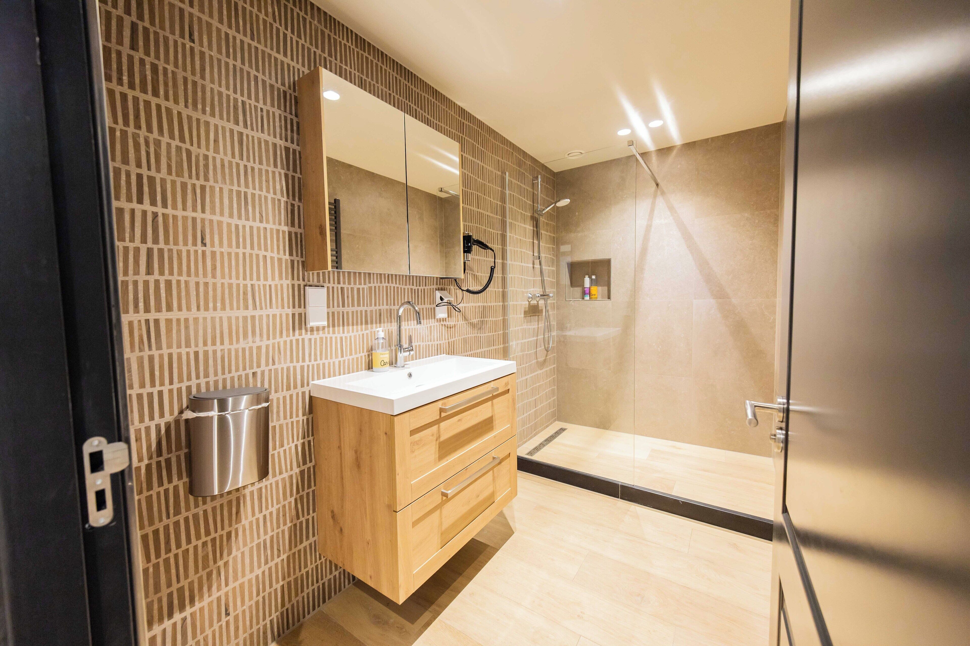 Een moderne badkamer met een houten wastafelmeubel, een grote spiegel en een douchecabine van glas.