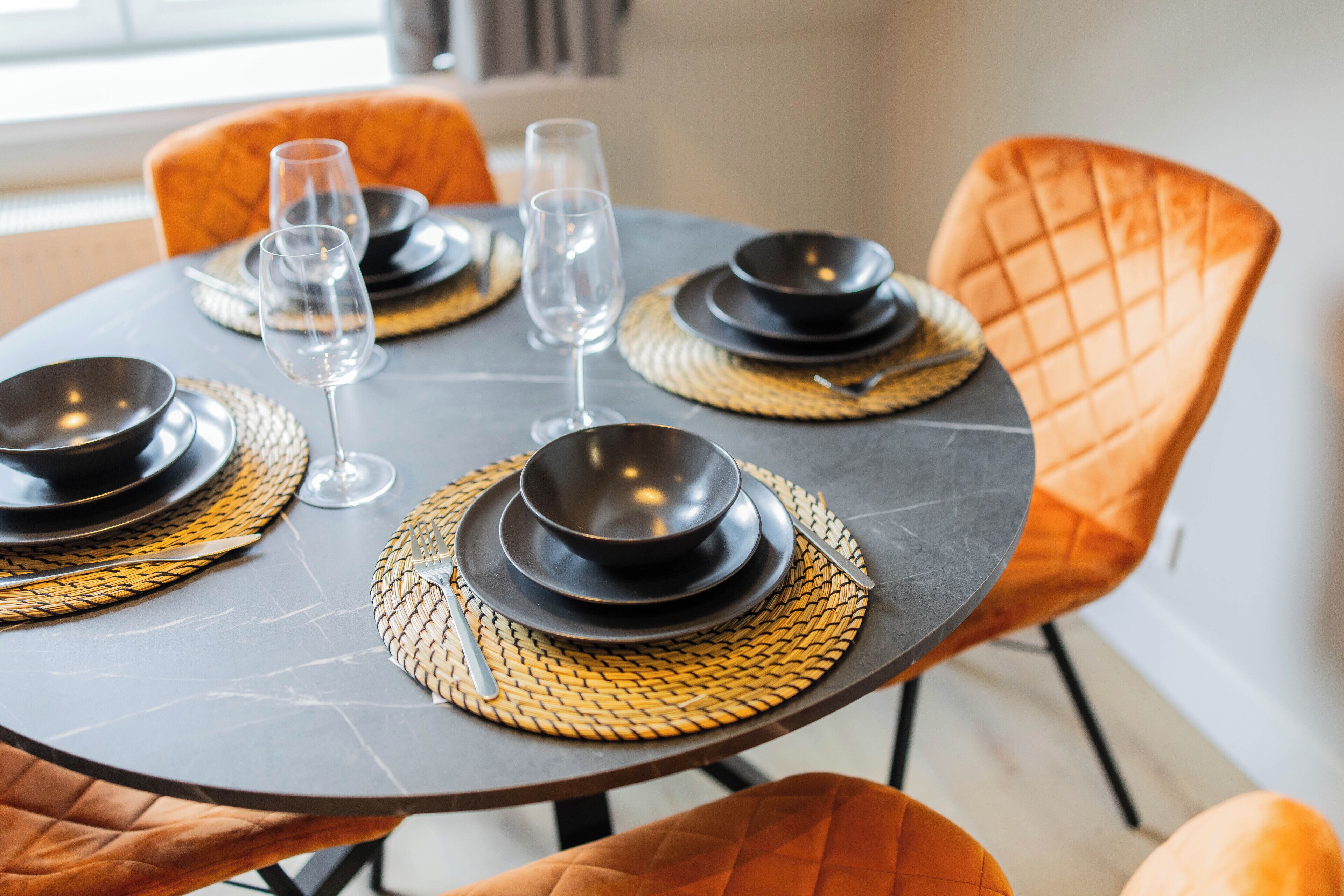 A dining table set with black plates, clear glasses, and woven placemats.