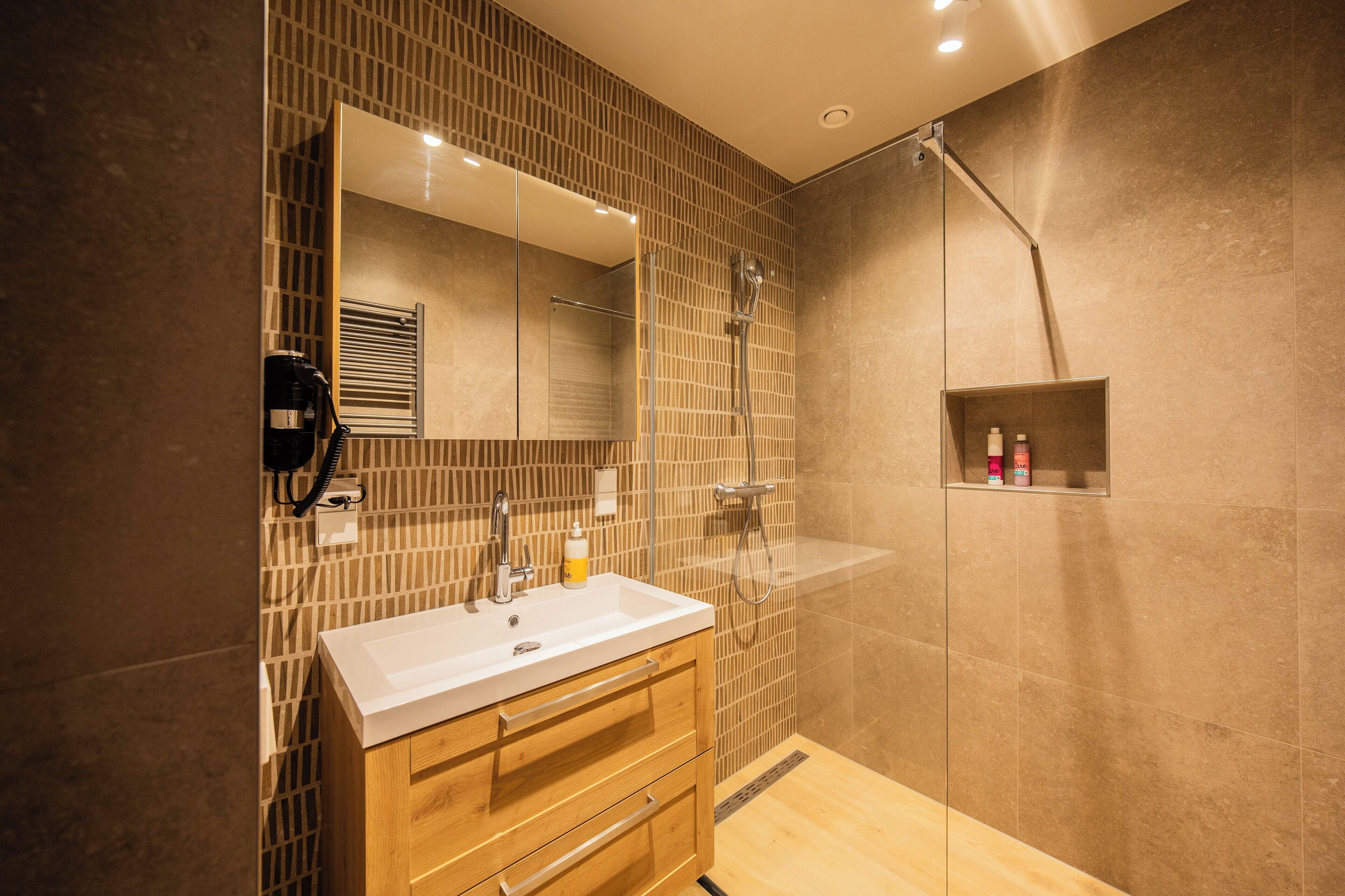 Un baño moderno con un espejo grande, un lavamanos, armarios de madera y una zona de ducha.
