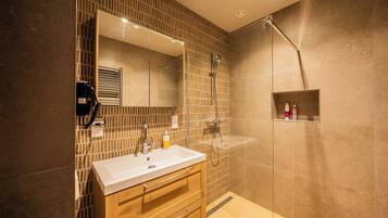 Un baño moderno con un espejo grande, un lavamanos, armarios de madera y una zona de ducha.