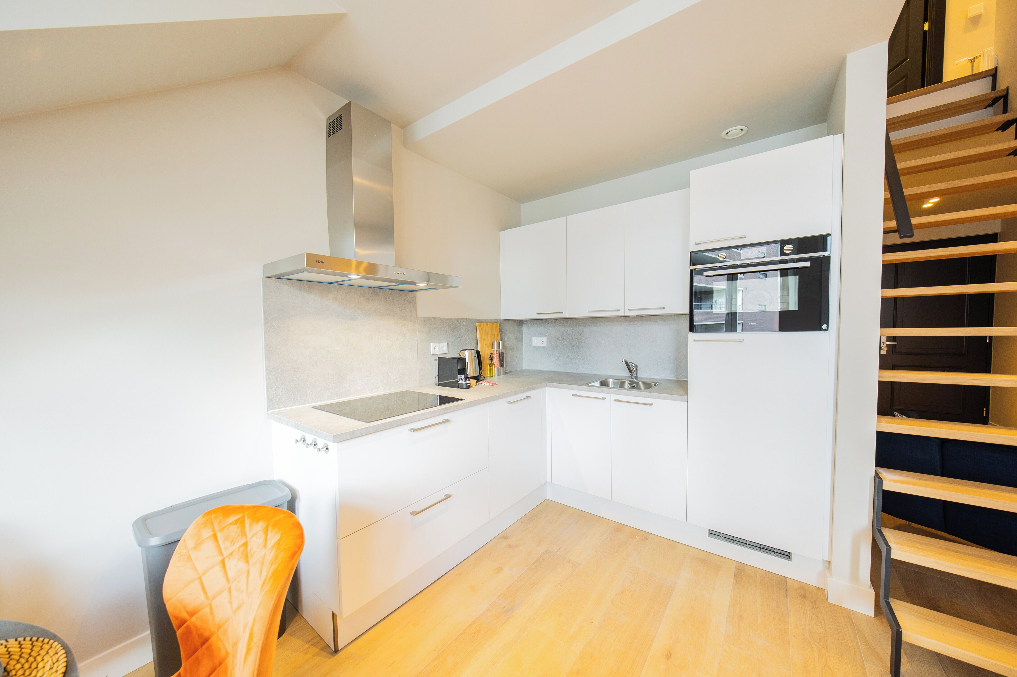 Una cocina moderna con armarios blancos, un horno de acero inoxidable y una escalera de madera.